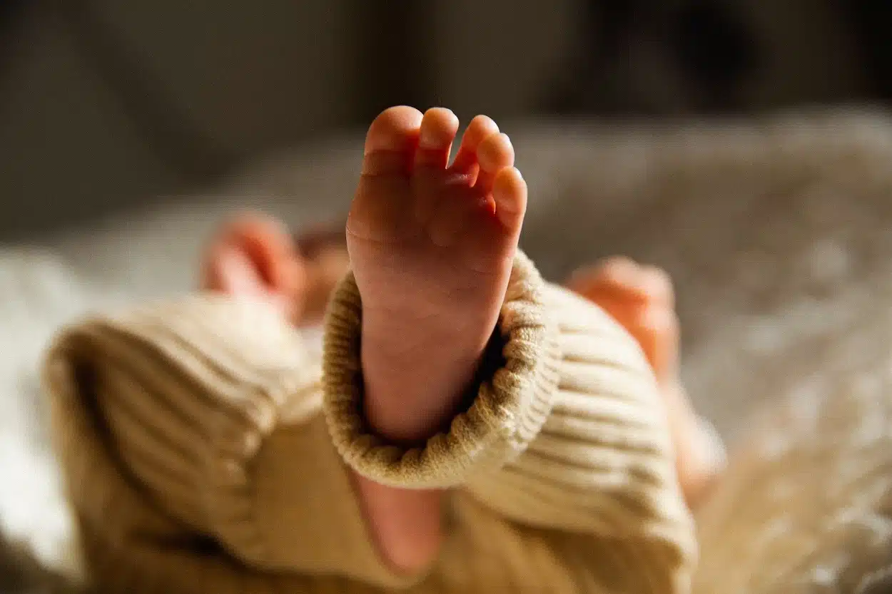 Em primeiro plano, pé esquerdo de um bebê, deitado sobre uma cama