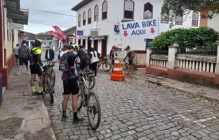 Bicicletas e ciclistas, em primeiro plano. Ao fundo, outros ciclistas e bicicletas, abaixo deuma faixa branca, com dos dizeres LAVA BIKE AQUI, na edição de 2021 do Iron Biker