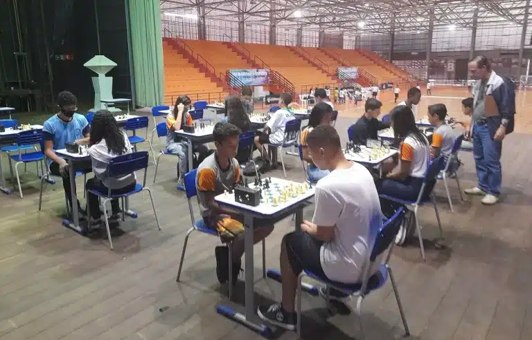 No palco da Arena MJovens estudantes disputam partidas de xadrez, nos Jogos Escolares de Mariana, em mesas colocadas no palco da Arena Mariana
