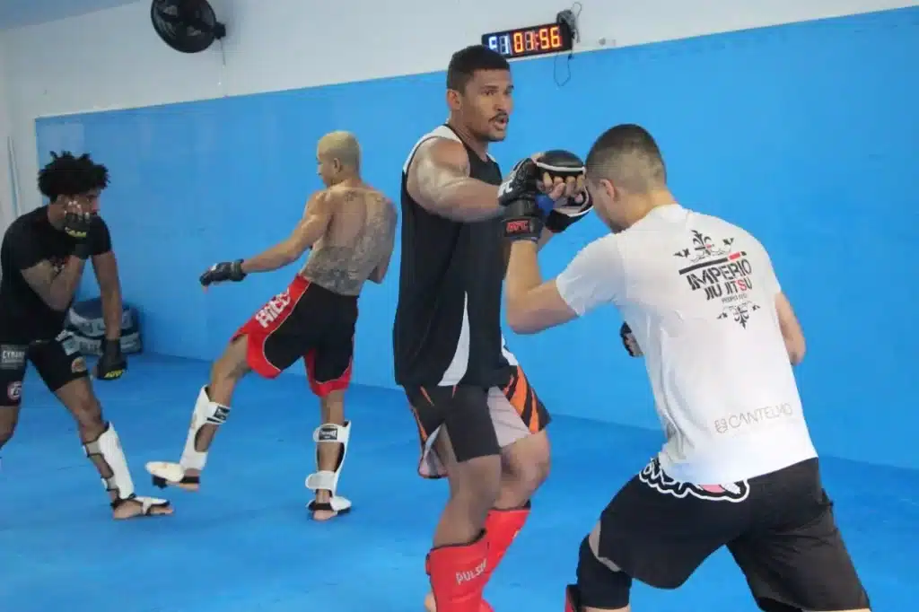 Em local com piso e paredes revestidas com borracha azul, 4 lutadores de MMA fazem treinamento de kickboxing
