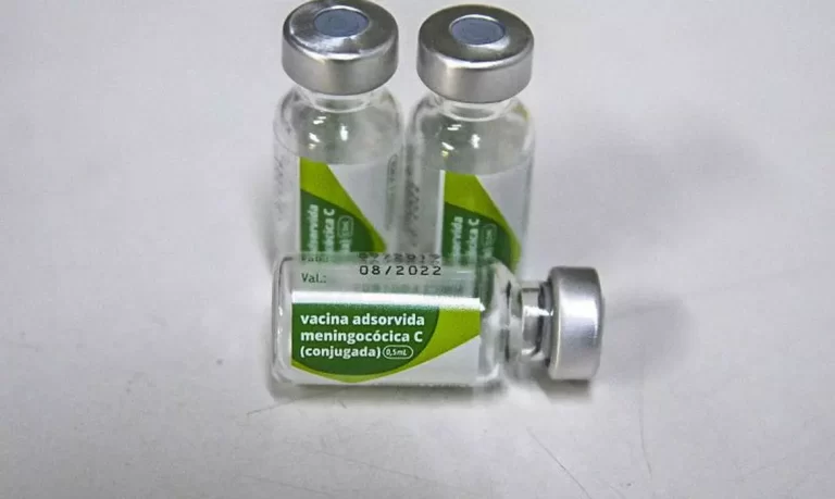 Três frascos de vacina contra a meningite C, sobre fundo infinito cinza