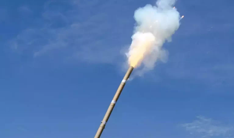 Com céu azul ao fundo, fogo de artifício é queimado, produzindo fumaça