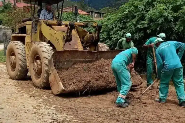 Trator da Secretaria de Obras é carregado por trabalhadores que recolhem lama em estrada