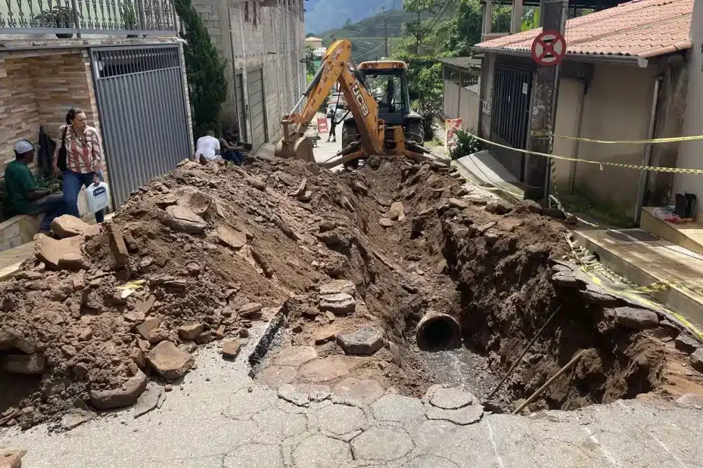 Equipamento da Prefeitura em trabalho de reparo de problema na rede de escoamento pluvial em rua do distrito de Passagem de Mariana